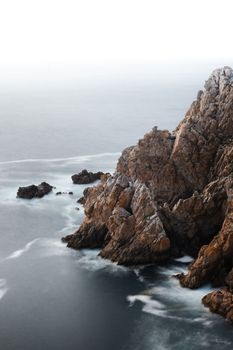 A stunning rocky coastline with dramatic cliffs and waves captured from above.