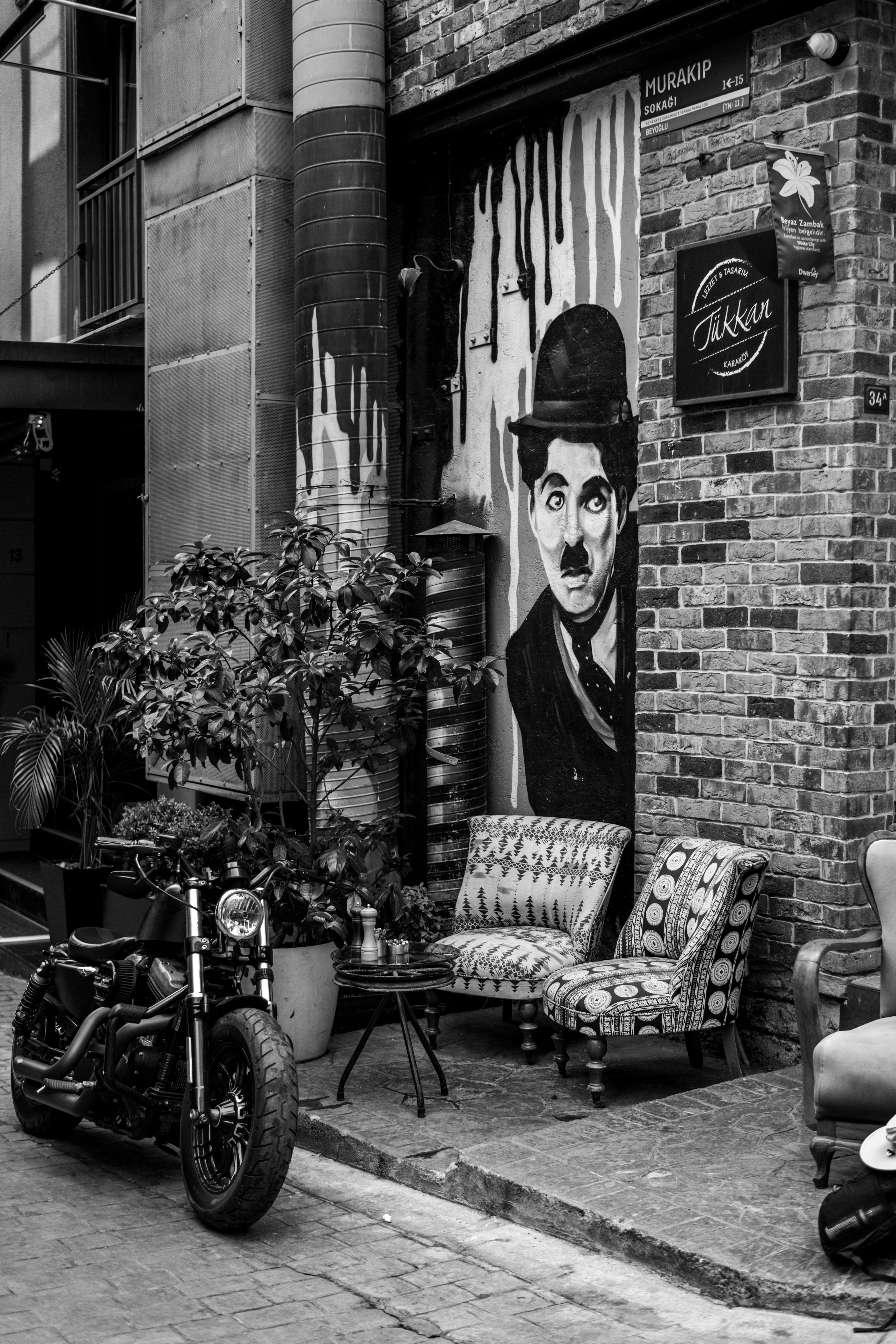 Black and white photo of İstanbul street featuring mural, motorcycle, and seating area.