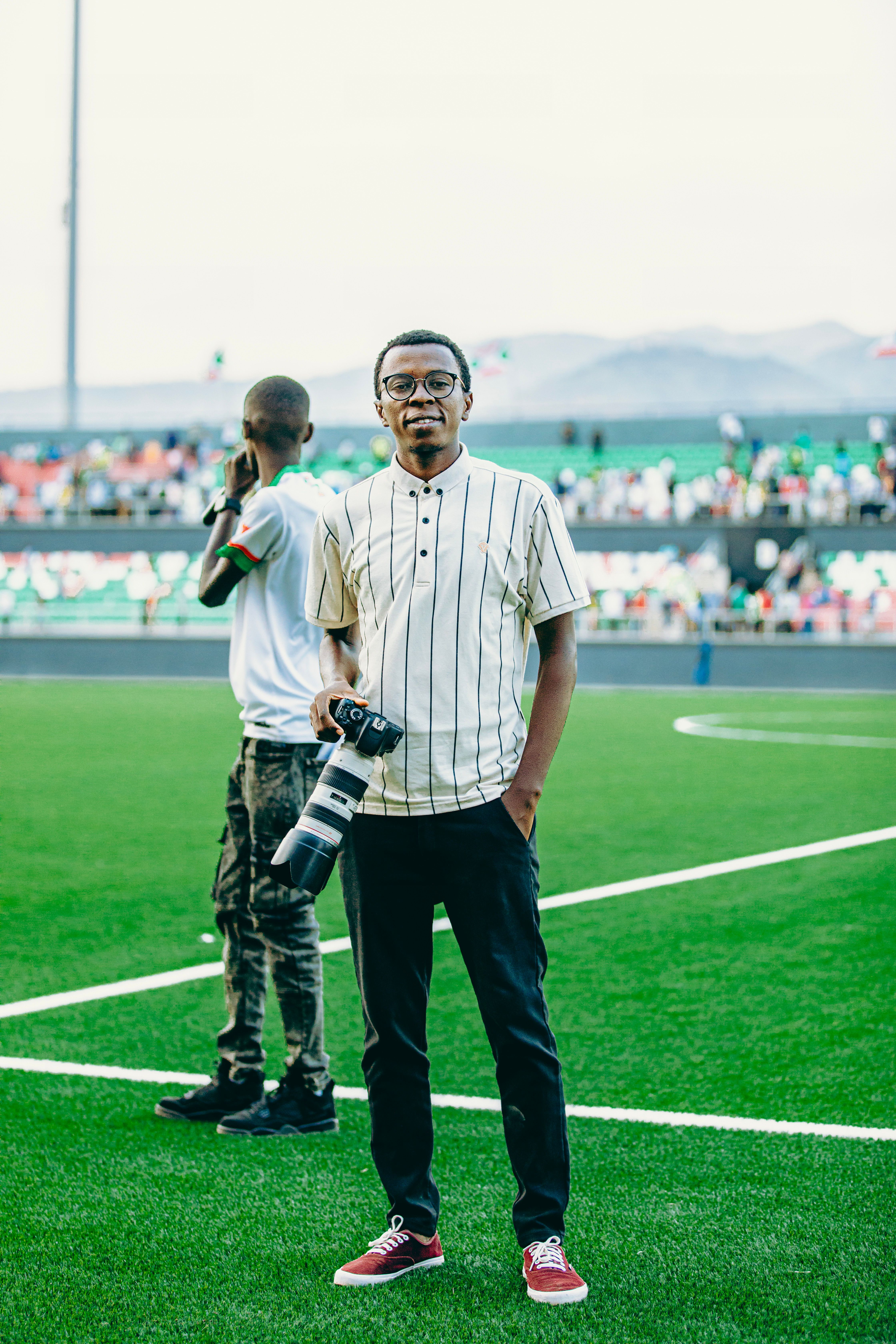 Photographer holding camera on a vibrant football field during a daytime sports event.