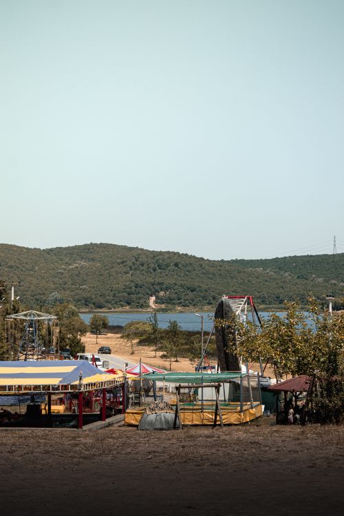 Free Vibrant fairground scene by a calm lake with rolling hills in the background. Stock Photo