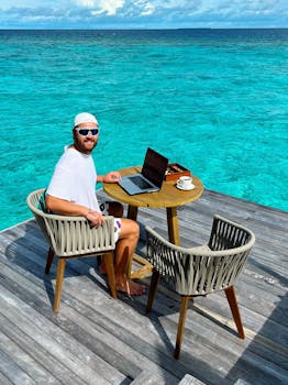 Man working on a laptop by the ocean, embodying remote work lifestyle.