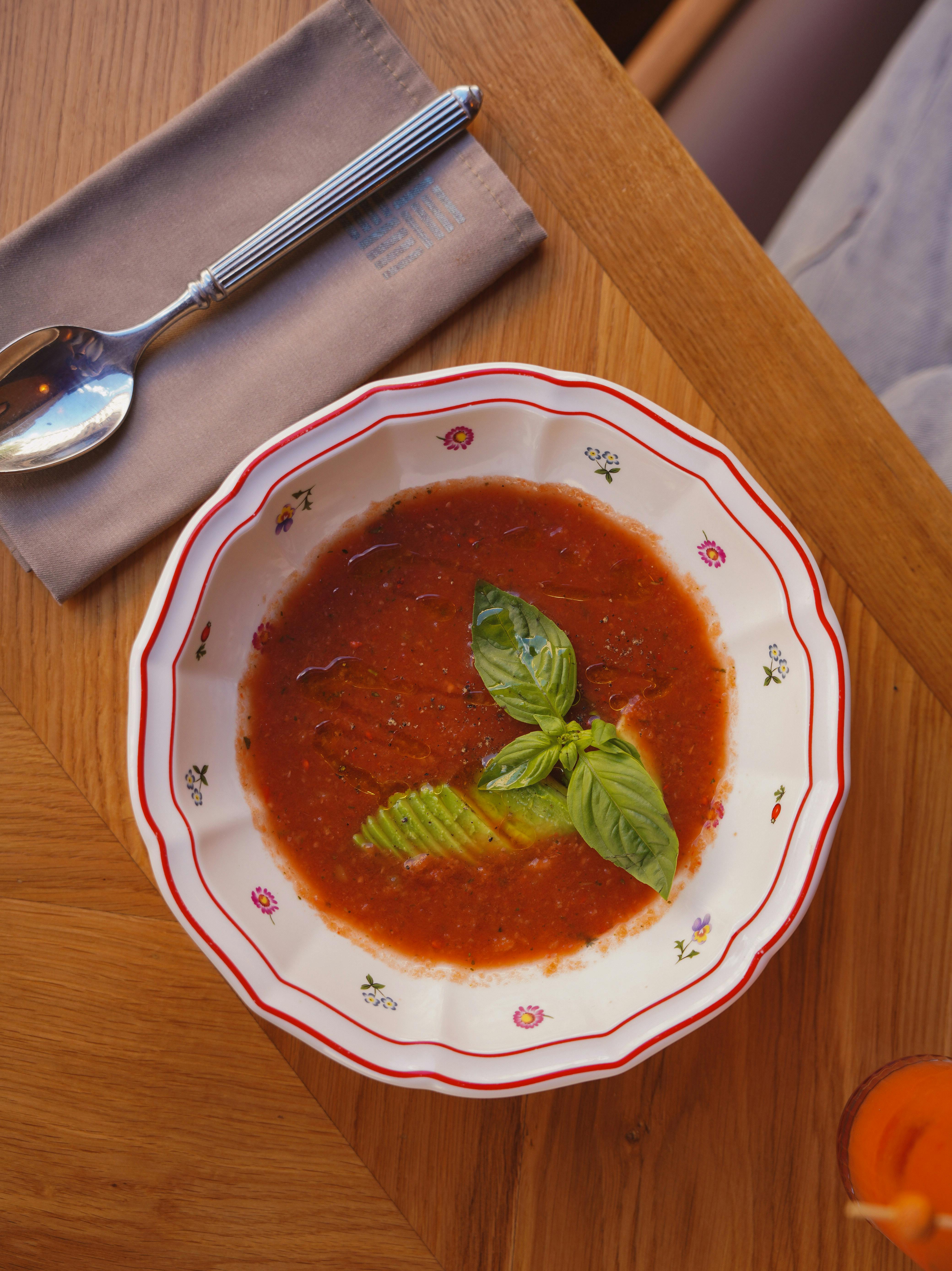 A vibrant tomato soup served in a decorative bowl with fresh basil, ideal for food enthusiasts.