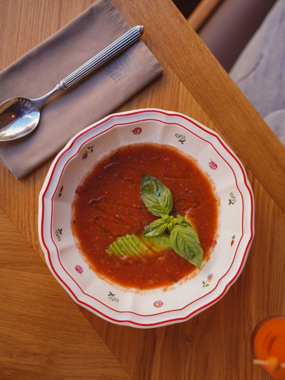 Chilled red gazpacho with fresh basil leaves and a fanned avocado in a floral bowl