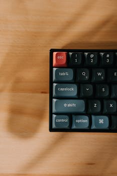 Top view of a mechanical keyboard with a red escape key on a wooden desk.