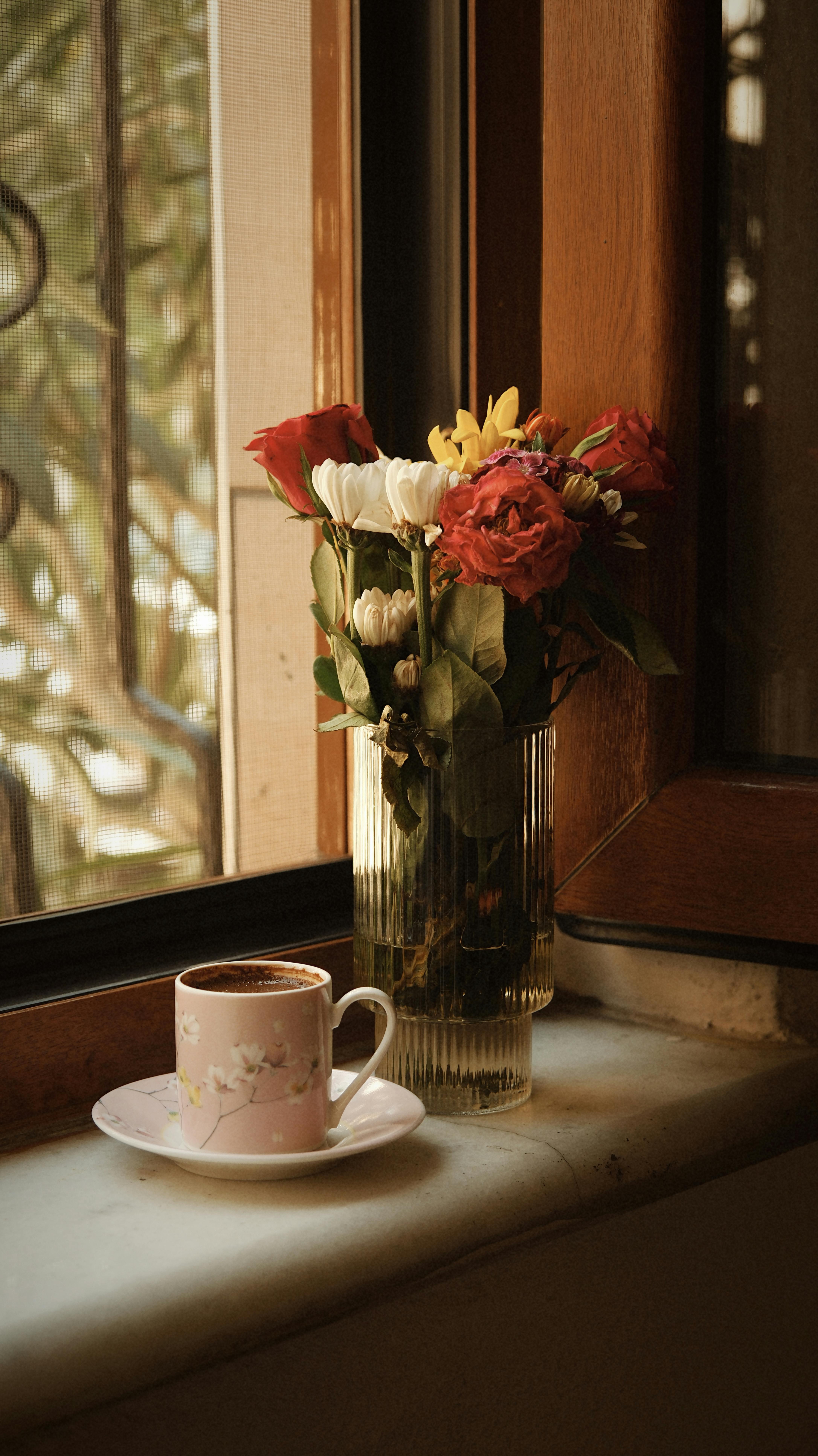 A warm cup of coffee with flowers by a window in soft morning light.