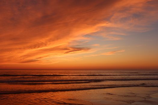 A breathtaking beach sunset with vivid orange and blue hues reflecting on gentle ocean waves.