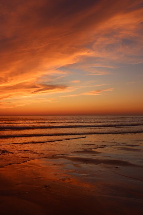 Free A breathtaking view of a sunset casting vibrant colors over quiet ocean waves and sandy beach. Stock Photo
