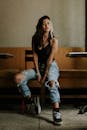 穿着破洞牛仔裤和运动鞋的时尚年轻女子在室内椅子上摆姿势，展示休闲时尚的风格