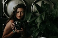 一位女士手持即时相机，周围是郁郁葱葱的深绿色植物