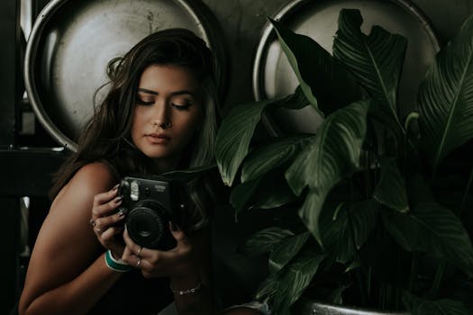 一个女人拿着即时相机，站在郁郁葱葱的深绿色植物中