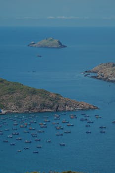 Aerial view of coastline with fishing boats and distant island in blue sea.