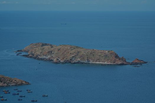 Aerial view of a rocky island and colorful boats in tranquil blue waters.