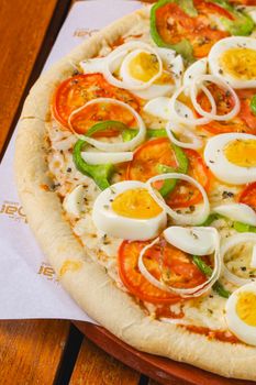 Close-up of a delicious homemade pizza topped with eggs, tomatoes, and green peppers on a wooden table.