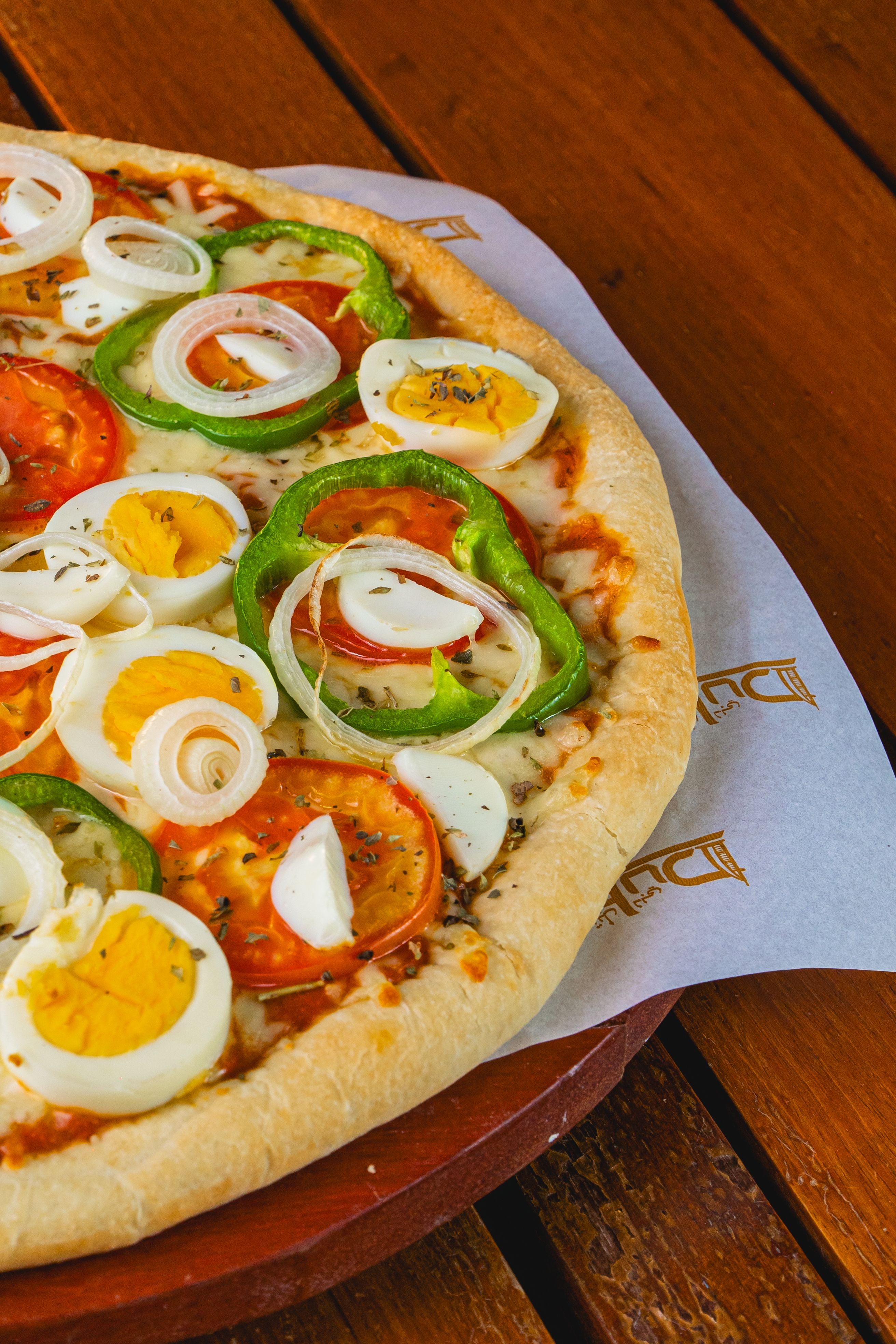 Close-up of a freshly baked pizza topped with eggs, tomatoes, and peppers on a wooden table.