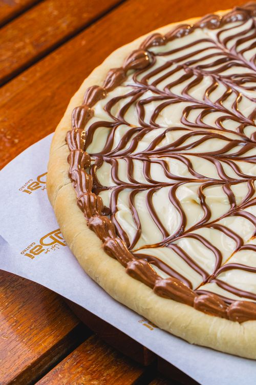Free Tempting dessert pizza topped with chocolate and vanilla sauce on a wooden table. Stock Photo