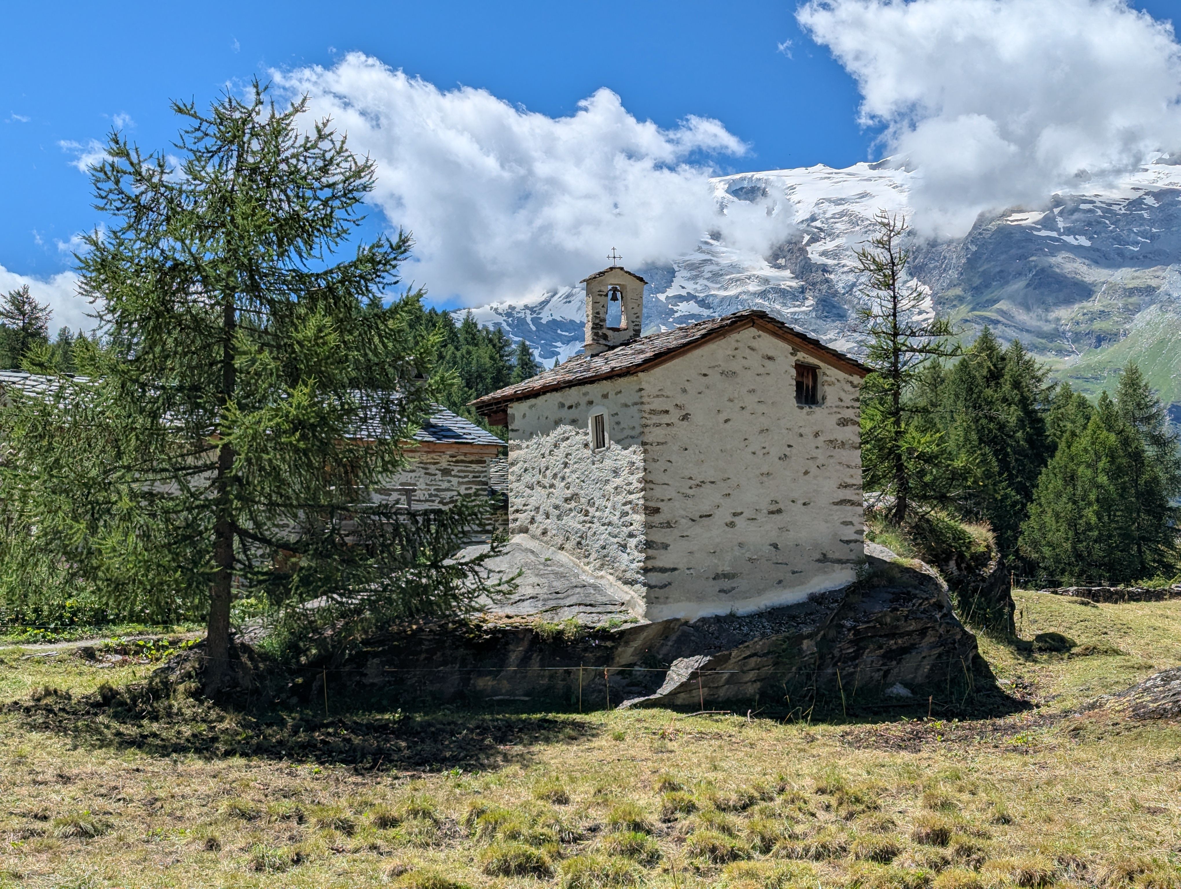 A serene stone chapel set against the backdrop of majestic snow-capped Alps on a sunny summer day. - Chamonix-Mont-Blanc