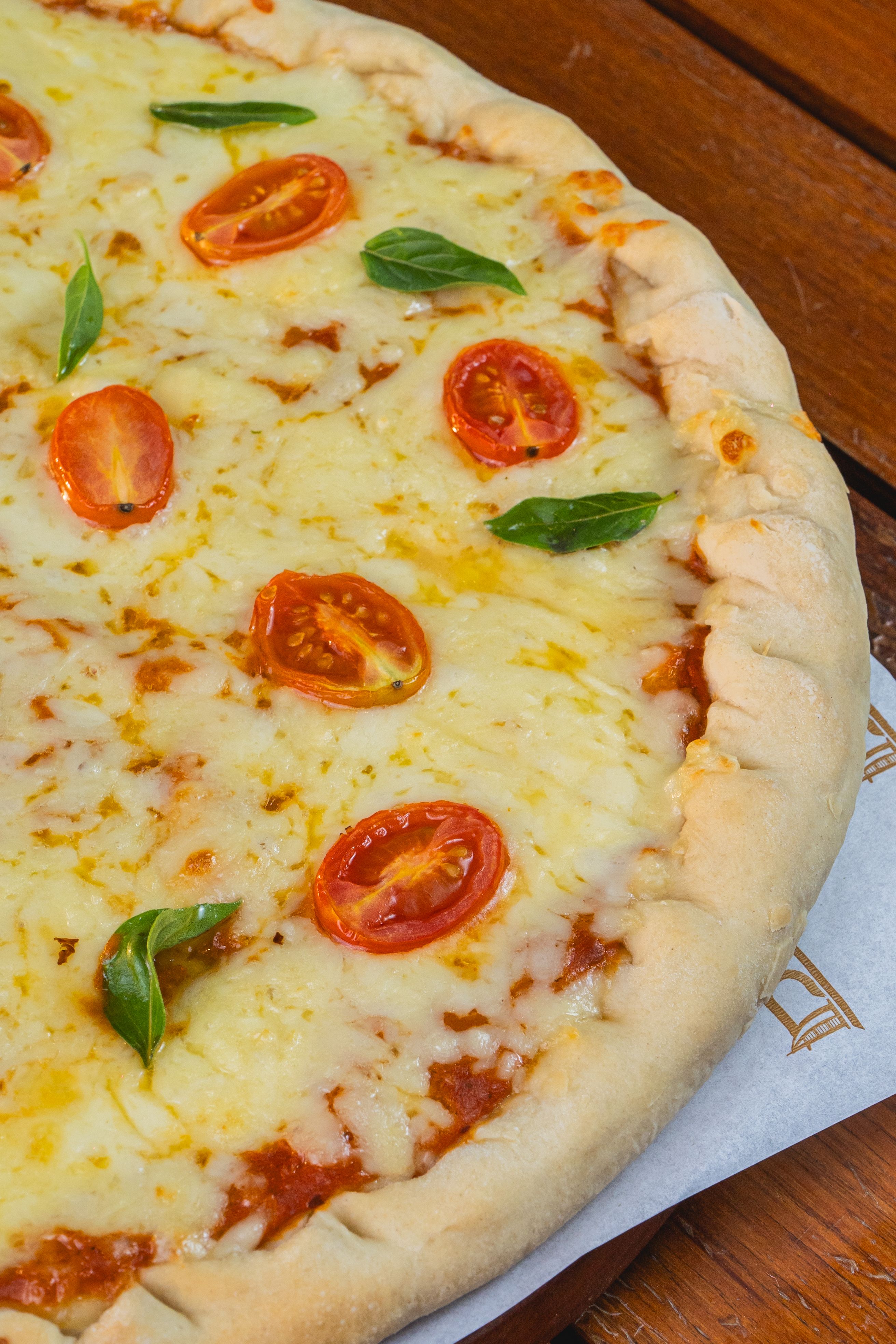 Close-up image of a cheese pizza topped with cherry tomatoes and basil on a wooden table.