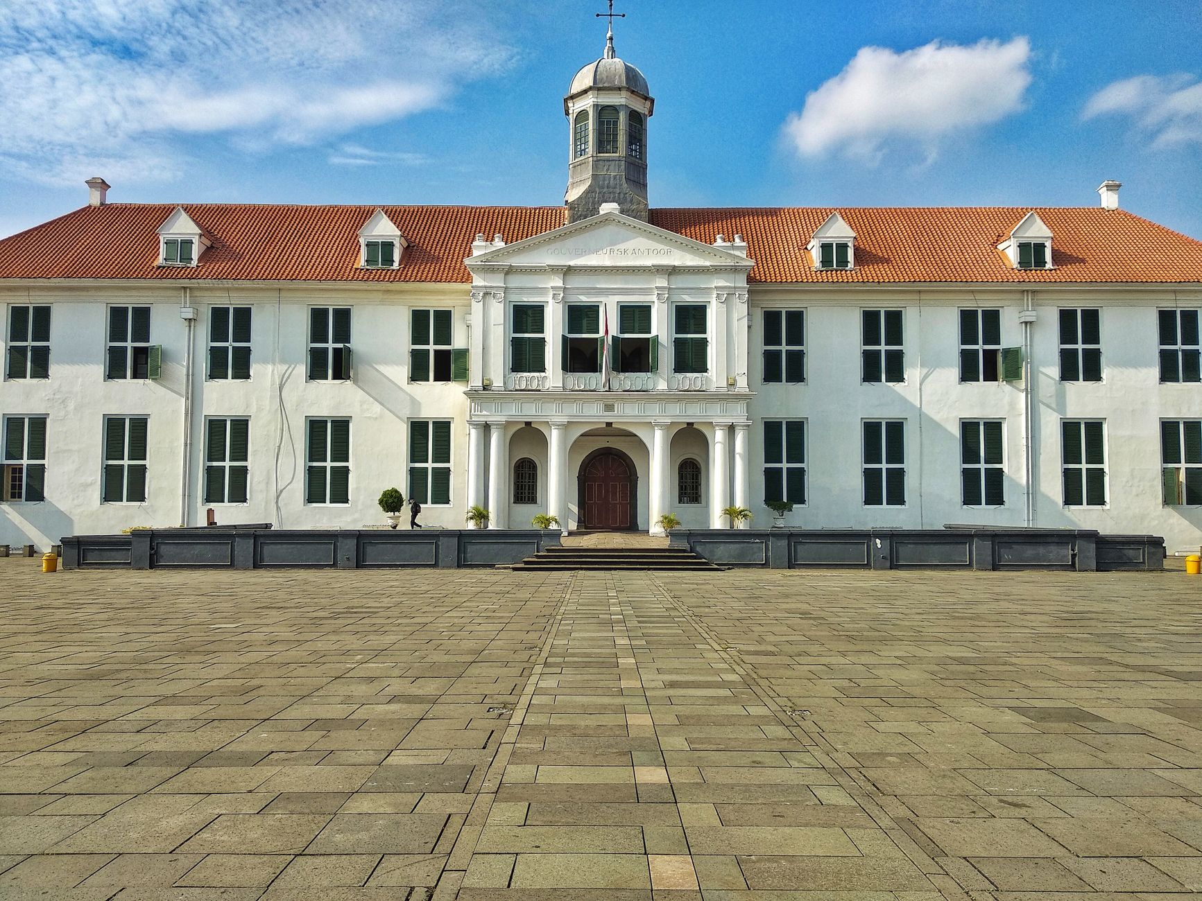 A grand colonial-style white building with a red roof against a blue sky.