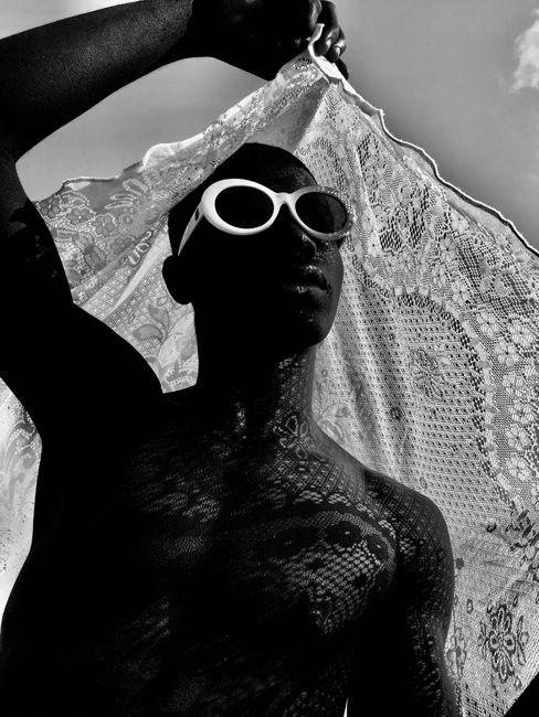 Artistic black and white portrait of a man with lace backlight and distinctive sunglasses, embodying style and contrast.