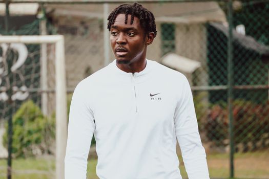 A young man in a white Nike jersey at an outdoor soccer field during the day.