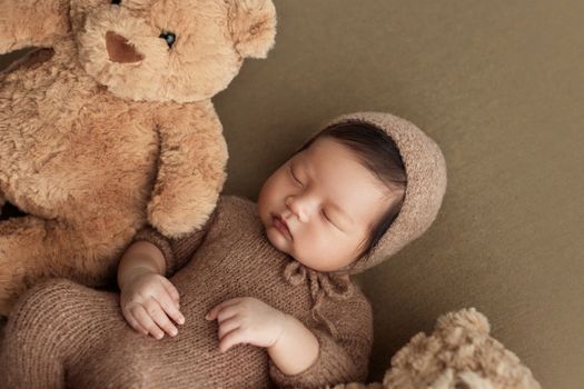 Cute newborn baby wearing knit outfit sleeping peacefully with teddy bears.