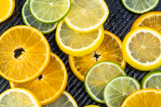 Fresh slices of citrus fruits, including oranges, lemons, and limes, displayed on a carbon background.