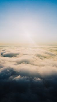 Peaceful aerial view of a serene sunrise above the clouds, showcasing a tranquil and expansive sky.