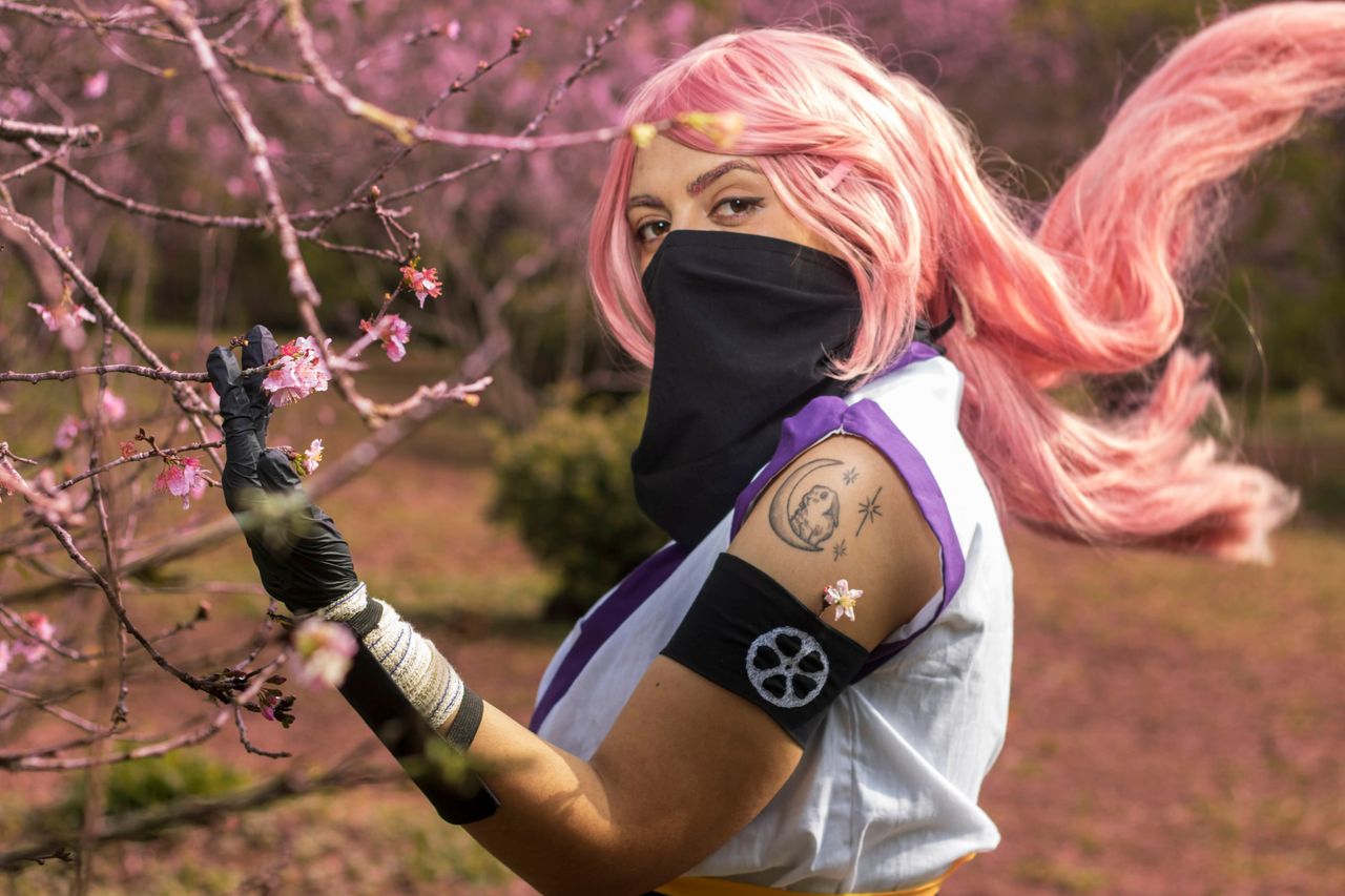 a cosplayer with pink hair poses amidst blooming cherry blossoms in a