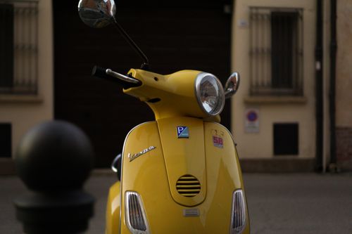Free A vibrant yellow Vespa scooter parked on a quiet street in Rimini, Italy. Stock Photo