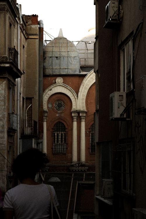 Free A shadowed alley reveals a historic red building's dome and arched windows. Stock Photo