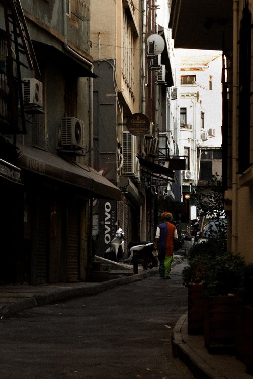Free Mysterious urban alleyway with a lone clown in vibrant attire, creating a dramatic scene. Stock Photo