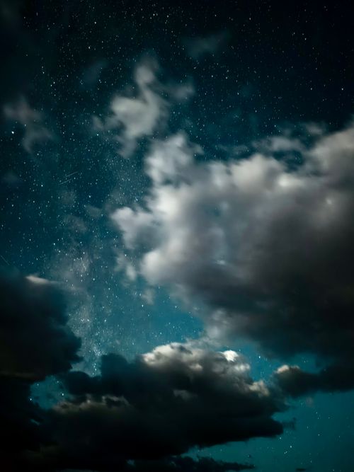 Free A stunning view of the night sky filled with stars and dramatic clouds, creating a serene atmosphere. Stock Photo