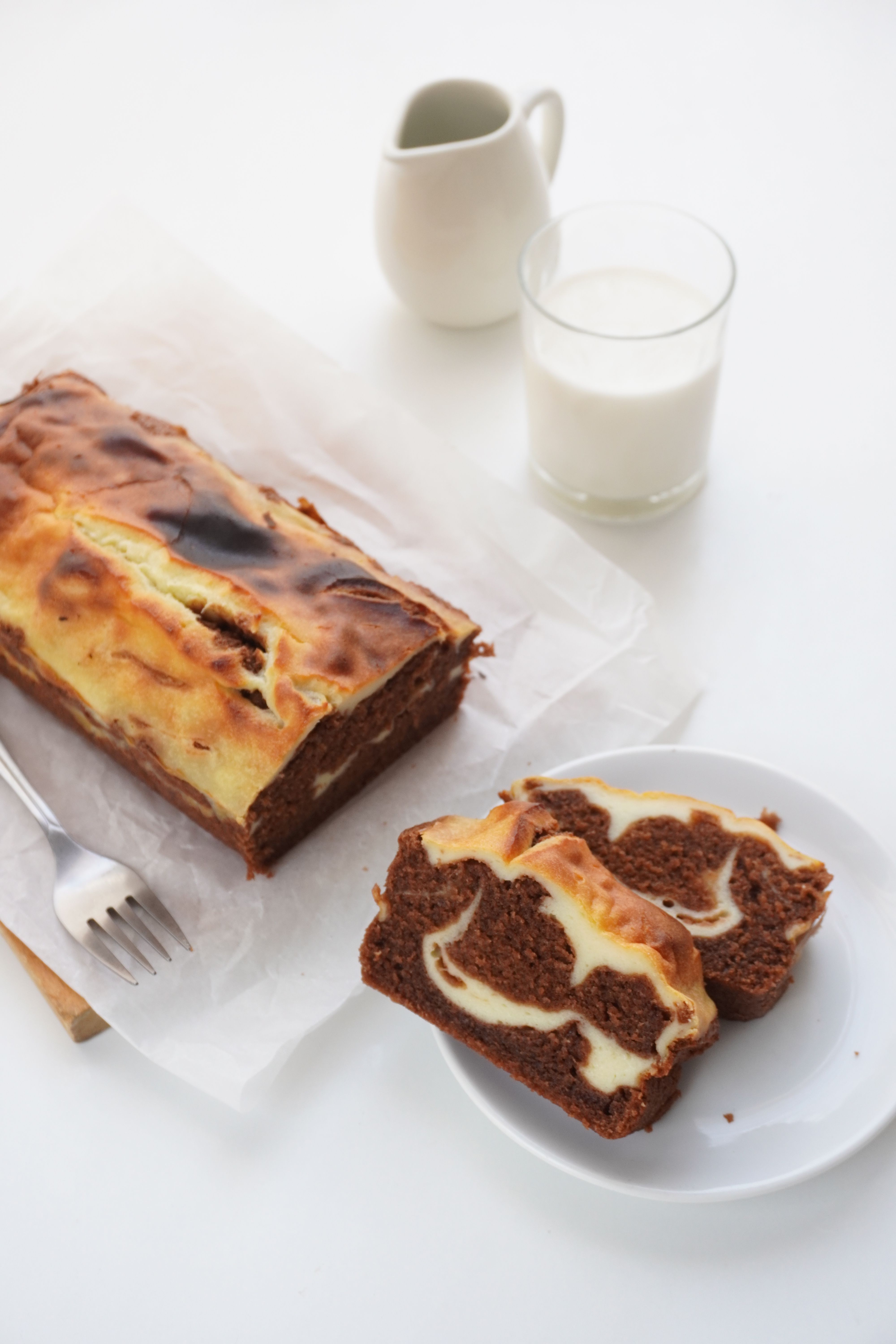 A sliced vanilla loaf cake on a wooden board showing a marbled dark chocolate swirl running through the pale crumb.
