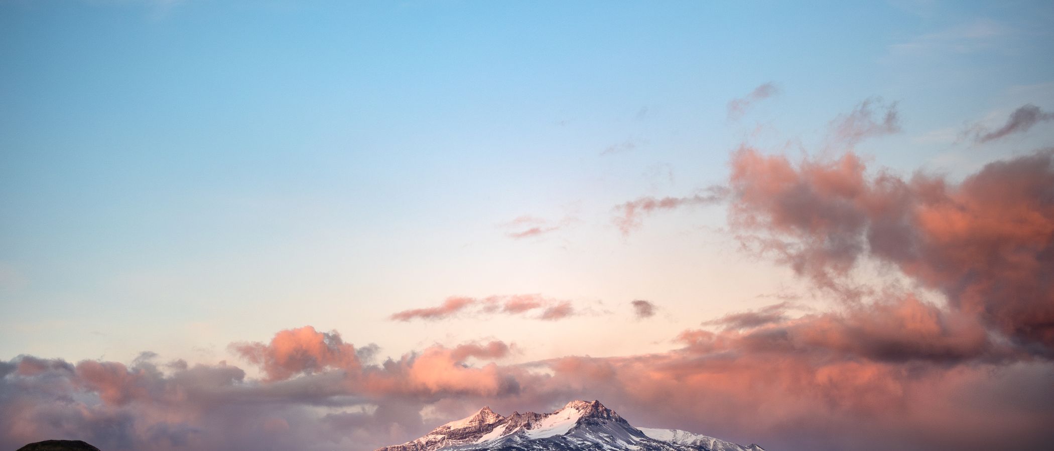 Sunrise light on snow-dusted Patagonian peaks beneath a band of pink cloud.