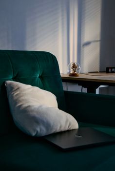 A cozy home office with green velvet sofa, pillow, and warm lighting, perfect for remote work.