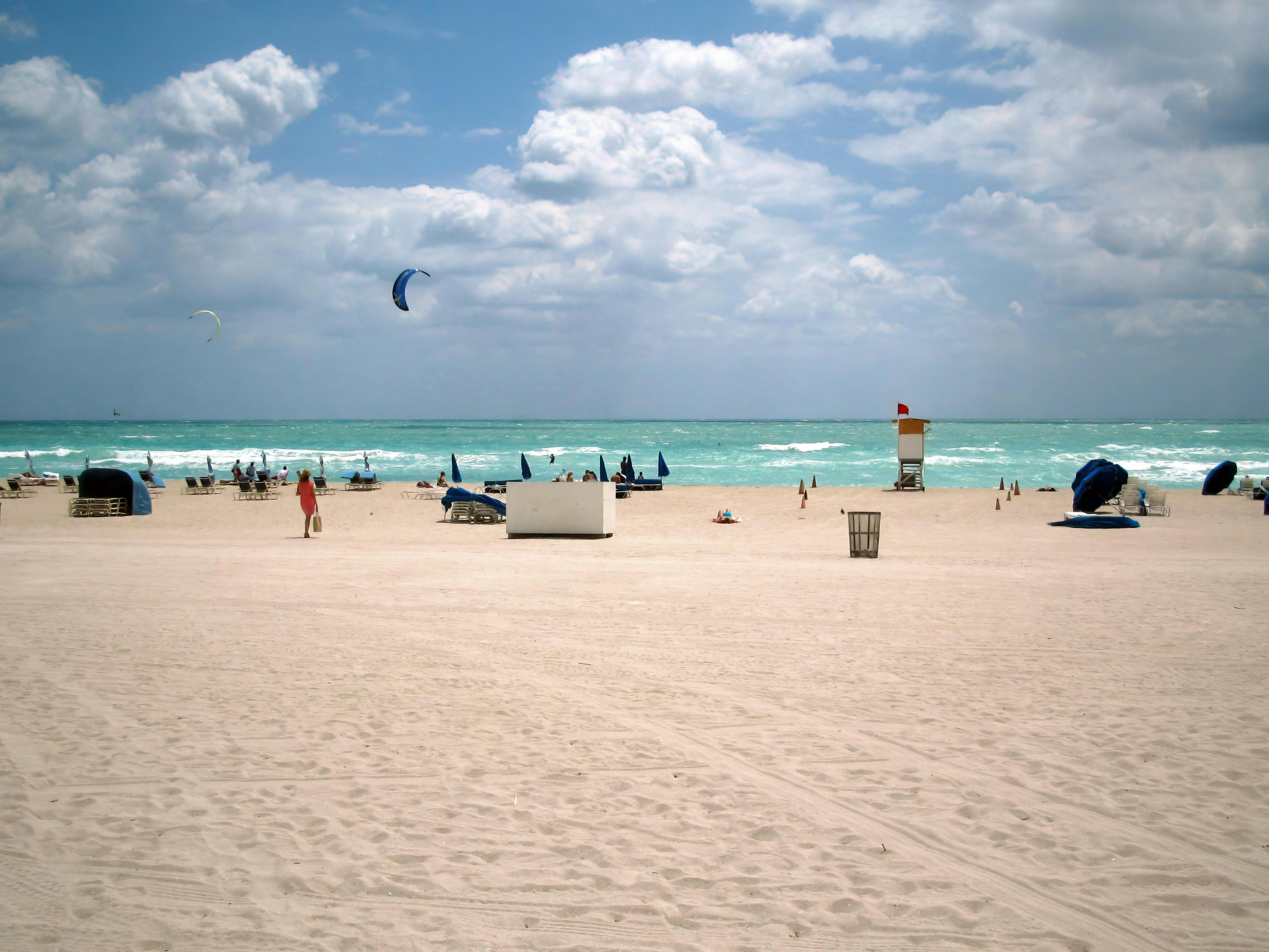 A vibrant beach scene in Miami Beach, Florida, showcasing kite surfers and beachgoers under a bright sky. - Miami