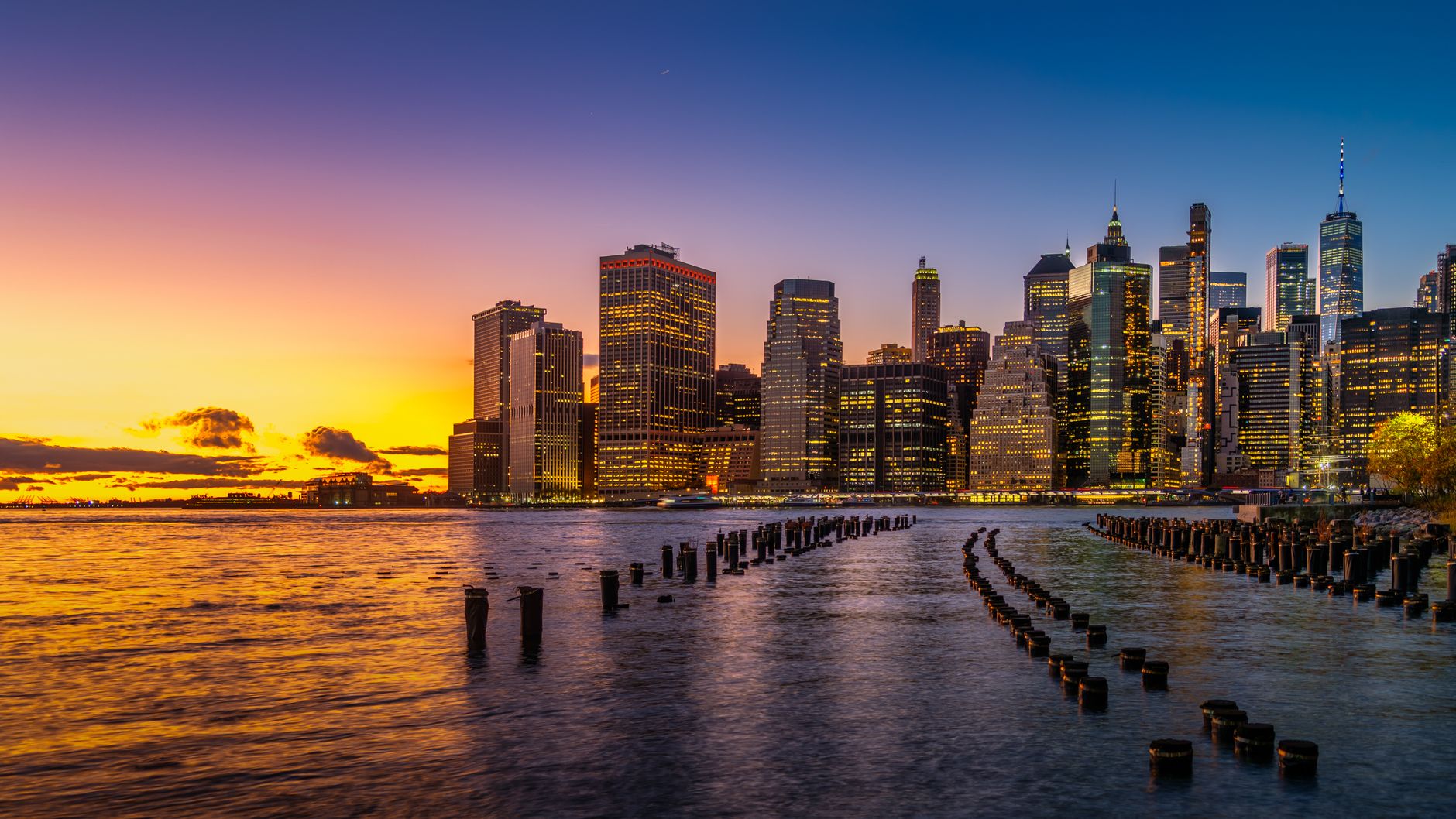 Breathtaking view of New York City's illuminated skyline during a vibrant sunset over the river.