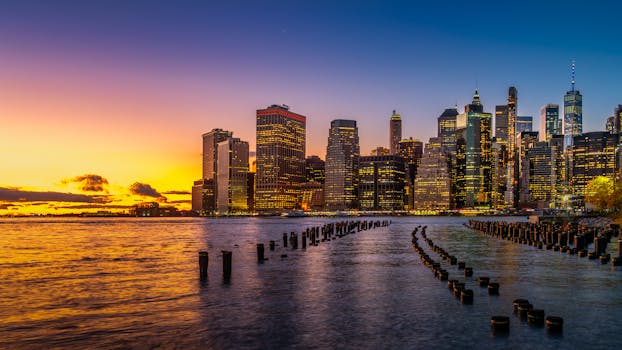 日落时分，纽约市灯火璀璨的天际线倒映在波光粼粼的河面上，景色壮丽