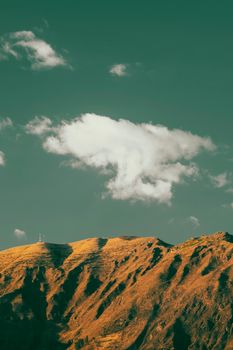 A peaceful mountain scene with a singular cloud floating above, casting a serene ambiance.