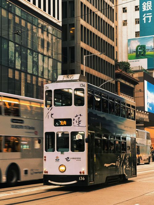 Free Double-decker tram navigating through bustling Hong Kong street surrounded by skyscrapers. Stock Photo