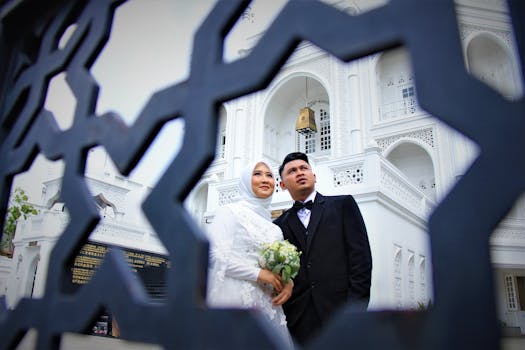 A wedding couple poses in front of a stunning white architectural landmark, framed by intricate patterns.