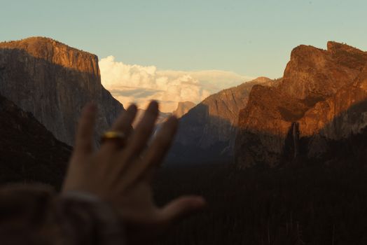 Golden hour view of Yosemite Valley with a hand reaching towards iconic cliffs.