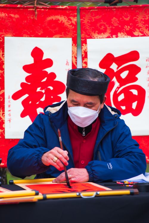 Free Masked artist practicing calligraphy outdoors with red banners. Stock Photo