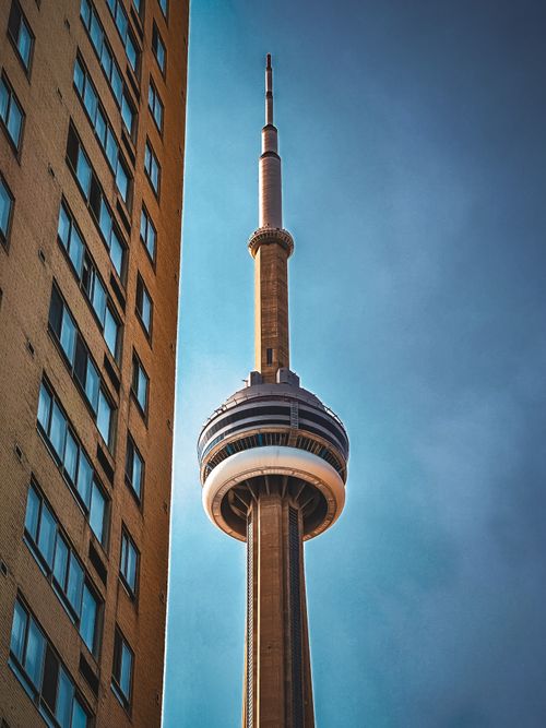 Free CN Tower rising majestically beside a city building under a clear blue sky in Toronto. Stock Photo