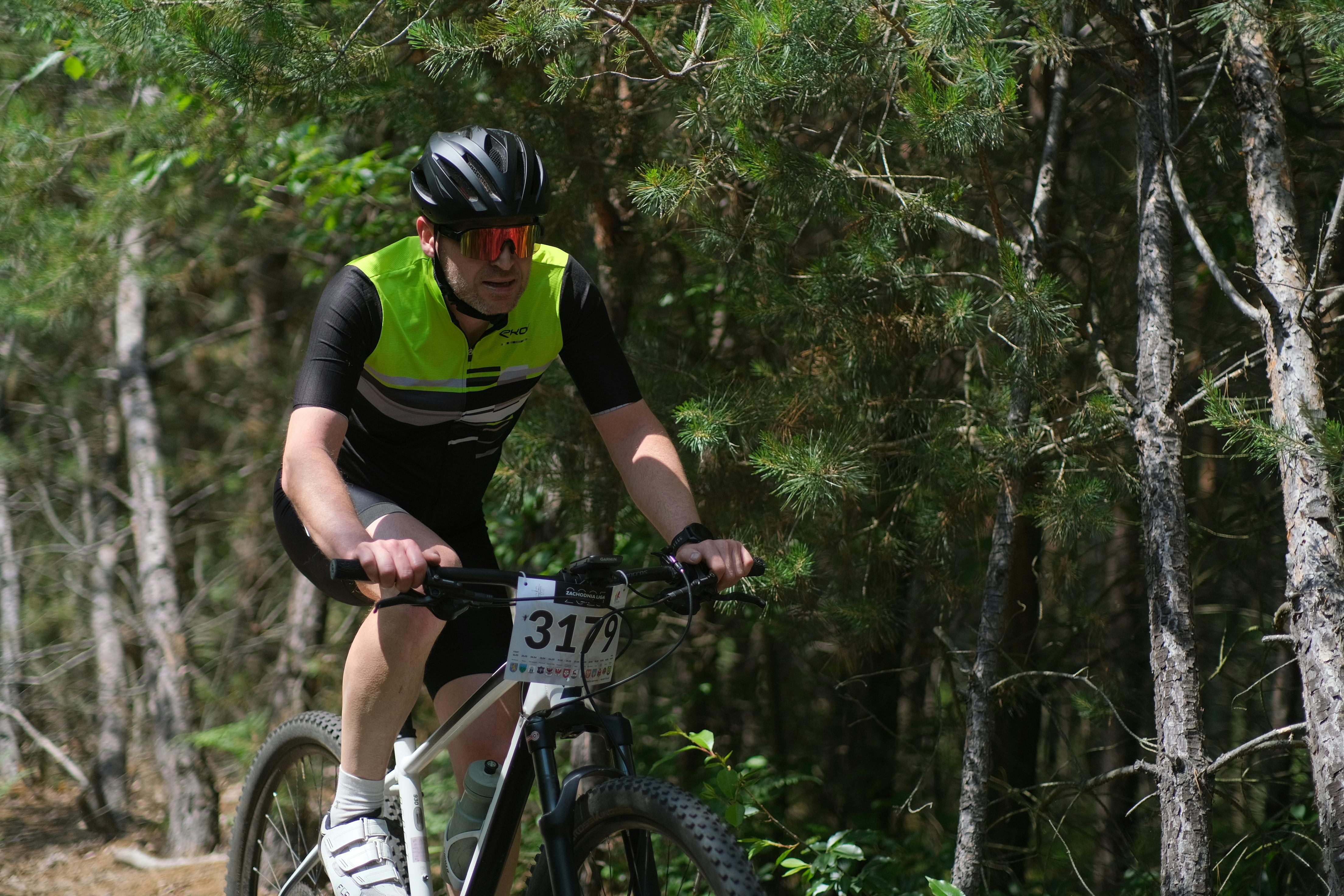 A male cyclist rides a mountain bike on a forest trail during a daytime race.