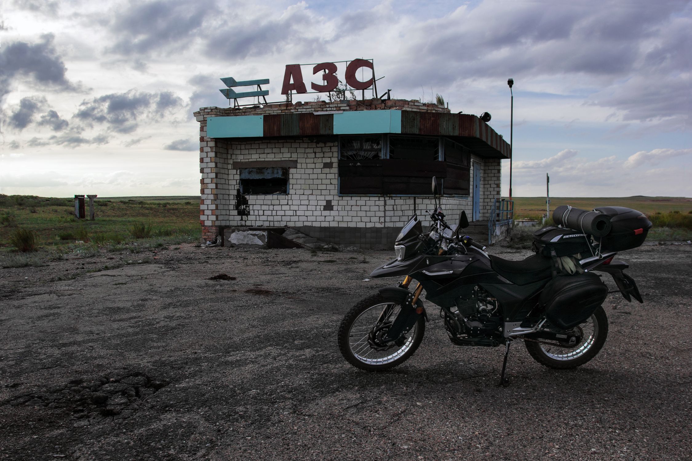 Explore adventure with a motorcycle parked at an abandoned rural gas station under a cloudy sky.