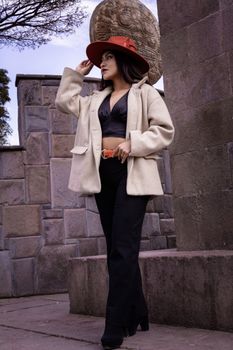 Fashionable woman in elegant attire posing near urban stone structure.