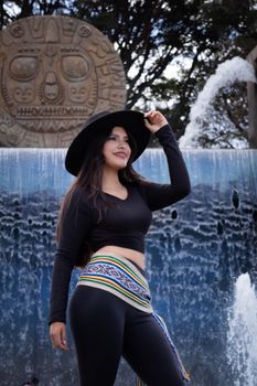 Smiling woman posing by a decorative fountain wearing a black hat and colorful scarf.