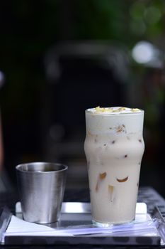 Close-up of iced coffee in a glass with cream on a tray, outdoors setting.