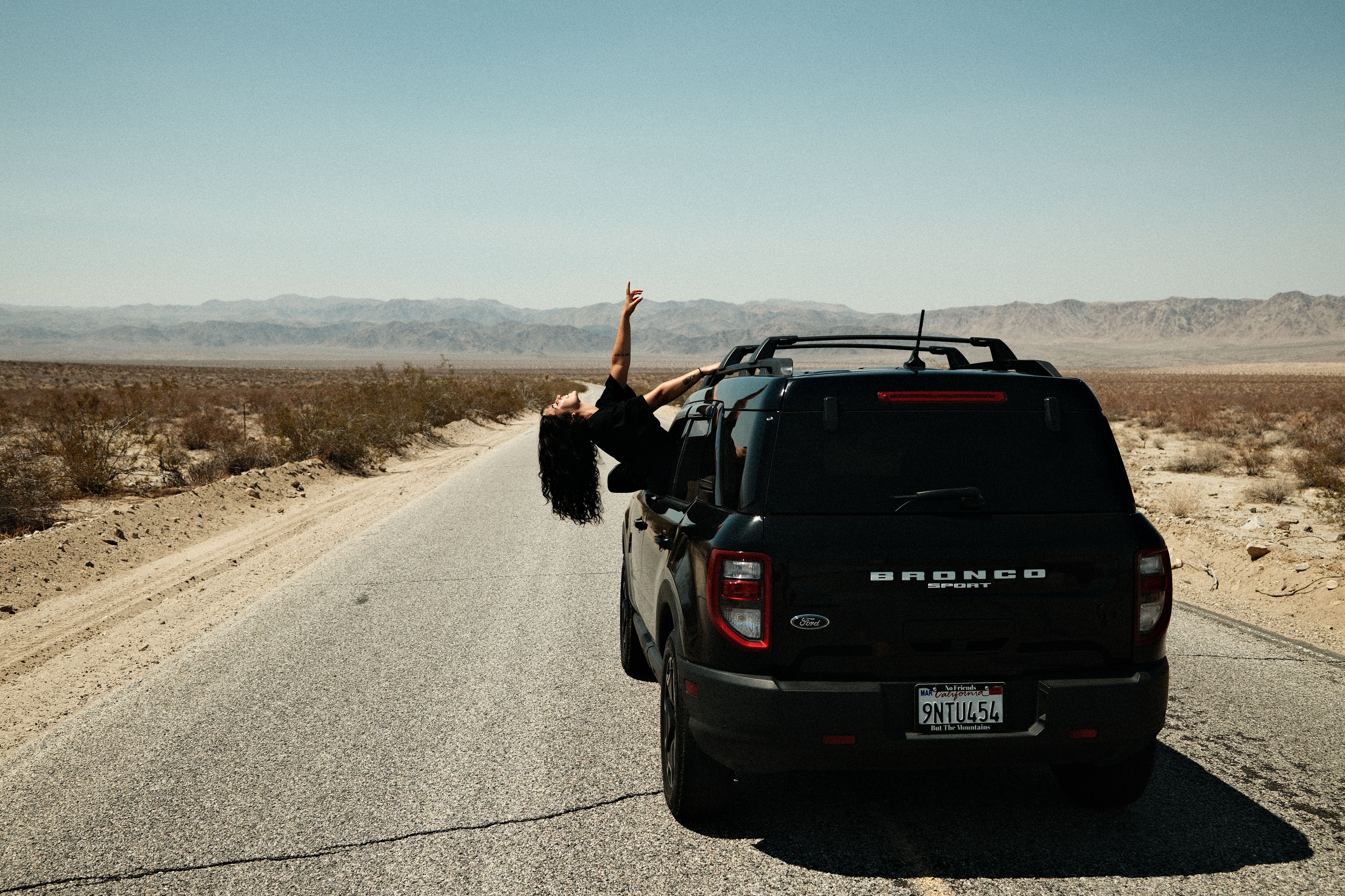 Woman stretching outside a car in a sunny desert landscape at Joshua Tree National Park.